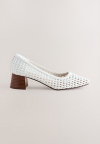 Witte geweven schoen met blokhak, puntige neus en houten hak. Heeft een open geweven ontwerp voor ademend vermogen en lichte textuur.