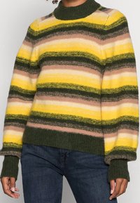 Sweter w paski z wysokim kołnierzem w odcieniach żółtego, zielonego i brązowego. Tekstura wełniana i ściągacze u mankietów. Posiada szerokie poziome paski.