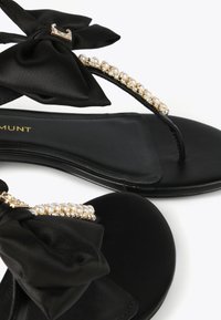 Black flip-flop sandals featuring a satin bow, pearl accents, and gold-tone hardware on a smooth sole. Simple and elegant design.