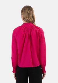 Fuchsia bluse med lange ærmer, der har en samlet ryg og elastiske manchetter. Glat tekstur, moderne design og rund halsudskæring.