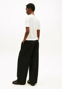 Biały sweter o fakturze z krótkim rękawem zestawiony z szerokimi czarnymi spodniami. Modelka stoi z rękami w kieszeniach, prezentując luźny krój i sylwetkę.