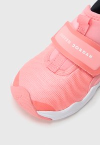 Ροζ αθλητικό παπούτσι με υφασμάτινο επάνω μέρος, λουράκι με βέλκρο, λευκή σόλα και διακριτικές λεπτομέρειες λογότυπου. Στρογγυλερή μύτη και μαλακός σχεδιασμός για άνεση.