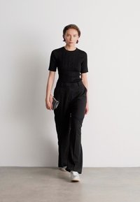 Juodas prigludęs trumpomis rankovėmis viršus derinamas su aukštu juosmeniu juodomis kelnėmis ir baltomis sportinėmis bateliais, sukuriant šiuolaikišką monochrominį įvaizdį.