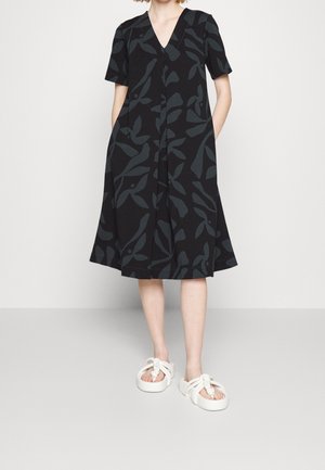 Sort kjole med korte ærmer, V-hals, med mønster af mørkegrå blade, A-formet silhuet og sidelommer. Kombination med hvide knudede sandaler.