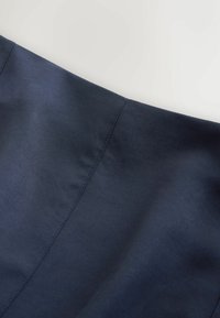Tissu bleu foncé avec couture visible sur une surface lisse, présenté sur un fond gris clair.