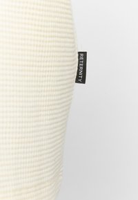 Wit, textiel kussen met een zwarte "RETERNITY" label zichtbaar aan de zijkant, dat een eenvoudig en modern ontwerp toont.