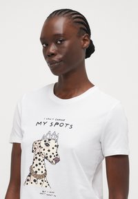 White cotton t-shirt featuring a cartoon of a spotted dog wearing a crown, with printed text above and below the image.