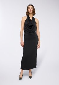 Abito nero con scollo a halter, corpo drappeggiato, silhouette aderente e tessuto morbido e elasticizzato, abbinato a tacchi a punta scintillanti.