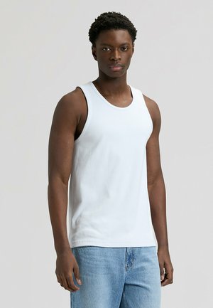 Hvid ribstrikket tanktop lavet af blød bomuld med rund halsudskæring og brede skulderstropper, kombineret med lyseblå jeans.