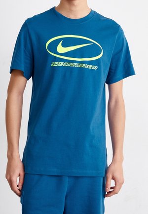 Blue cotton T-shirt featuring a round neckline and short sleeves. Front graphic includes a green Nike logo and text "NIKE SPORTSWEAR."