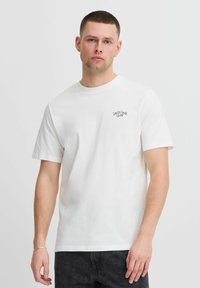 Balta medvilnės marškinėliai trumpomis rankovėmis ir apvalia iškirpte. Ant krūtinės yra mažas juodas išsiuvinėtas "Danish Fashion Club" logotipas.