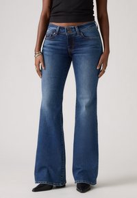 Jeans foncés évasés avec des détails délavés, design classique à cinq poches, fermeture à bouton et coupe ajustée à la taille.