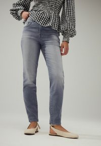 Jeans ajustados de color azul claro con un lavado desgastado, combinados con una blusa de cuadros en blanco y negro con mangas abullonadas. Zapatos planos beige.