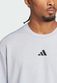 Felpa grigio chiaro con collo a giro, dotata di un logo Adidas nero sul petto. Tessuto morbido con una vestibilità rilassata.