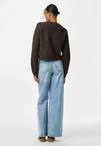 Suéter marrón de canalé, de longitud cropped; combinado con jeans de pierna ancha en azul claro; cuenta con bolsillos traseros y calzado casual de perfil bajo.