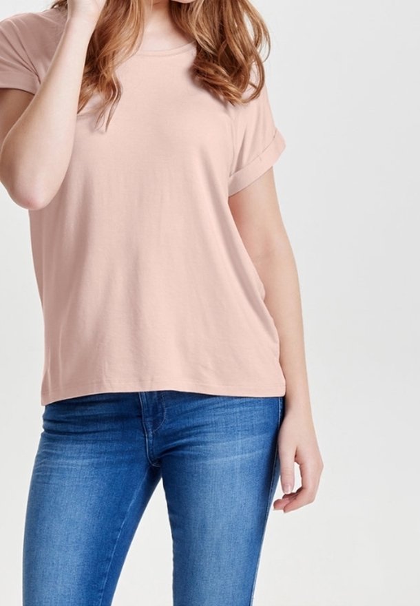 T-shirt rose pâle à manches courtes en tissu doux, doté d'une coupe décontractée avec des revers roulés, associé à un jean en denim bleu.