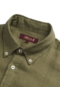 Camicetta verde oliva con colletto realizzata in tessuto testurizzato, caratterizzata da bottoni bianchi e un'etichetta bordeaux con il nome del marchio.