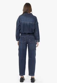 Completo in denim con giacca corta e ampia dal retro arricciato e pantaloni cargo dal taglio morbido, entrambi in un lavaggio blu scuro. Scarpe nere.