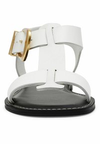 Sandal in pelle bianca con una fascia larga e una fibbia dorata. Presenta una suola nera liscia e una cucitura bianca a contrasto lungo il bordo.