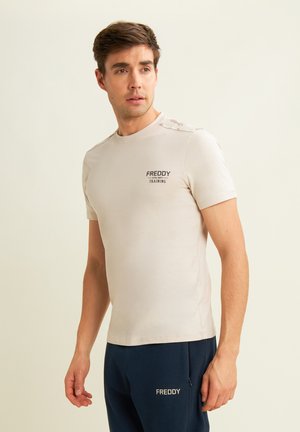 T-shirt beige a maniche corte con scollo rotondo e logo contrastante nero "FREDDY TRAINING" sul lato sinistro del petto. Tessuto liscio, design aderente.