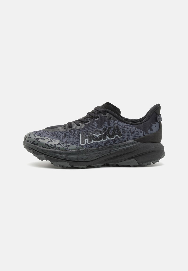 Zapatilla de correr negra con una parte superior de malla texturizada y suela de goma gruesa. Presenta un diseño estampado y un logo reflectante en el costado.