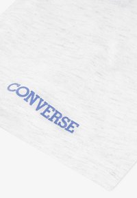 Vit bomullsduk med en subtil textur, med en blå "CONVERSE"-logotyp tryckt i fet stil längs den nedre kanten.