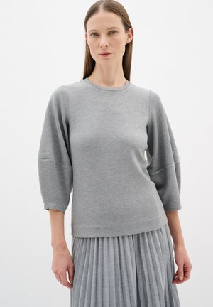 Grauer Pullover mit rundem Halsausschnitt und Dreiviertelärmeln, mit einer glatten Textur. Kombiniert mit einem grauen Faltenrock.