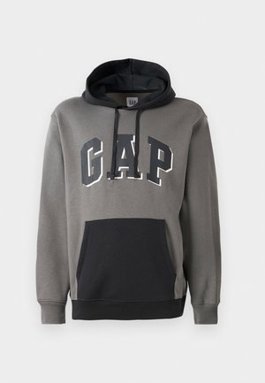Grå hettegenser med svart kengurulomme, har "GAP" logo i fet skrift over brystet, og justerbar hette.