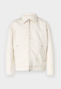 Chaqueta de mezclilla blanca con cuello puntiagudo, cierre de cremallera completa, bolsillos laterales y costuras en contraste. Presenta un corte relajado y un diseño minimalista.