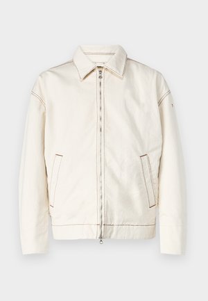 Balta džinsa jaka ar norādītu apkakli, pilnu rāvējslēdzēja aizdari, sānu kabatām un kontrastējošiem šuvju elementiem. Raksturīga brīvā piegriezuma un minimālistisks dizains.