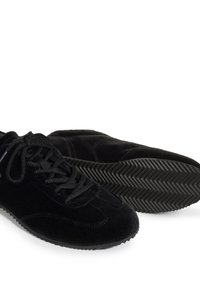 Paire de chaussures en daim noir à lacets avec semelles en caoutchouc texturées, une chaussure face vers le haut et l'autre montrant le motif de la semelle.
