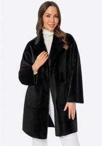 Abrigo de piel sintética negra con un amplio cuello, mangas largas y dos bolsillos frontales. Textura suave y diseño de longitud media, adecuado para un uso casual.