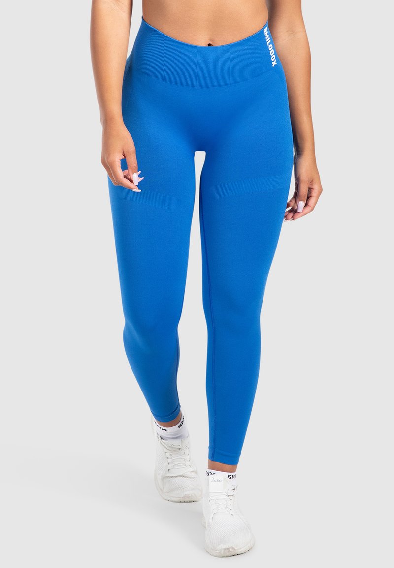 Leggings a vita alta, aderenti e di un vivace blu, con dettagli a coste sulla vita, abbinati a sneakers sportive bianche.