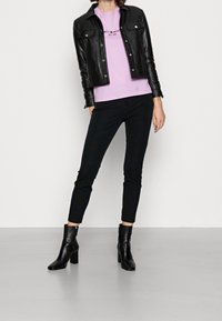 Svart läderjacka över en ljuslila t-shirt, kombinerad med svarta slim fit-byxor och svarta ankelboots med blockklackar. Enkel design.