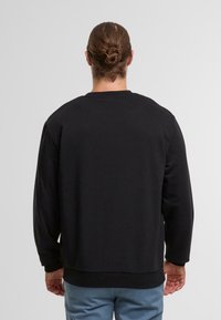 Zwarte sweatshirt met ronde hals, lange mouwen en geribbelde manchetten. Gladde textuur en een ontspannen pasvorm met een rechte zoom op de taille.
