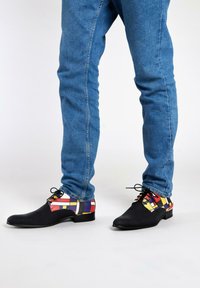 Zwarte leren schoenen met een kleurrijke geometrische print op de achterkant, met rode, gele en blauwe accenten. Suède textuur met vetersluiting.