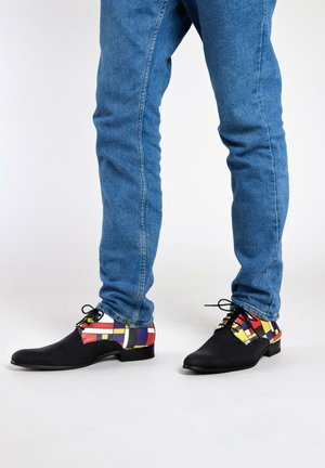 Zwarte leren schoenen met een kleurrijke geometrische print op de achterkant, met rode, gele en blauwe accenten. Suède textuur met vetersluiting.