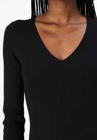 Black ribbed knit top with long sleeves and a deep V-neckline. The fabric appears soft and stretchy, featuring vertical ribbing for texture.