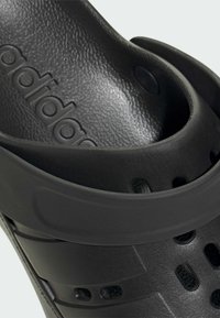 Sorte formede sandaler med en struktureret overflade, der har ventilationshuller og en tyk rem. Brandet med "adidas" prægede indeni.