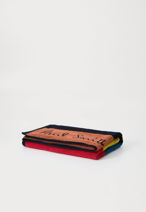 Serviette multicolore pliée en couches. Présente un dessus orange avec le texte "Paul Smith", des accents bleu foncé, rouge, vert et bleu. Texture douce.