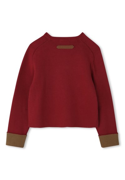 Un pull rouge avec un col rond, des manches raglan et des poignets marron. Présente une petite étiquette en cuir à l'arrière. Texture douce.