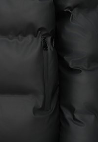 Černá péřová bunda s hladkou, matnou texturou a kapsou na zip vpravo, zdůrazňující prošívaný design.