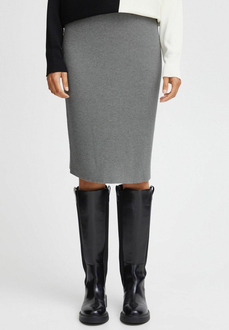 Person wearing a grey ribbed knit skirt, black and white color-block sweater, and knee-high black leather boots, standing on a white background.