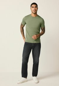 Zelené bavlnené tričko s krátkymi rukávmi a okrúhlym výstrihom, skombinované s tmavými džínsami a bielymi teniskami. Neformálny, priliehavý dizajn.