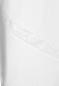 Bílá látka s diagonální ventilační mřížkou, ukazující jemnou pletenou texturu a detaily prodyšného sportovního materiálu.