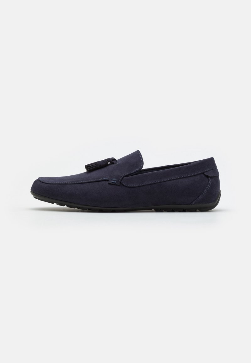 Mocassin en daim bleu marine avec détail de glands, style à enfiler, et semelle en caoutchouc noire, présenté en profil latéral sur fond blanc.