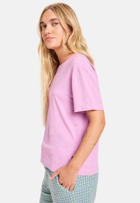Lichtroze T-shirt met korte mouwen gemaakt van zachte katoen. Klassieke ronde hals, lichte boxy fit en een eenvoudig ontwerp zonder versieringen.