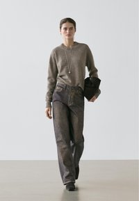 Pull en maille marron, jean large en denim foncé, collier en argent, sac à main noir et bottines. Palette de couleurs neutres, coupe décontractée.