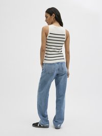 Top senza maniche a righe in crema e nero, abbinato a jeans a gamba larga blu chiaro. I jeans presentano dettagli strappati e una vestibilità comoda.