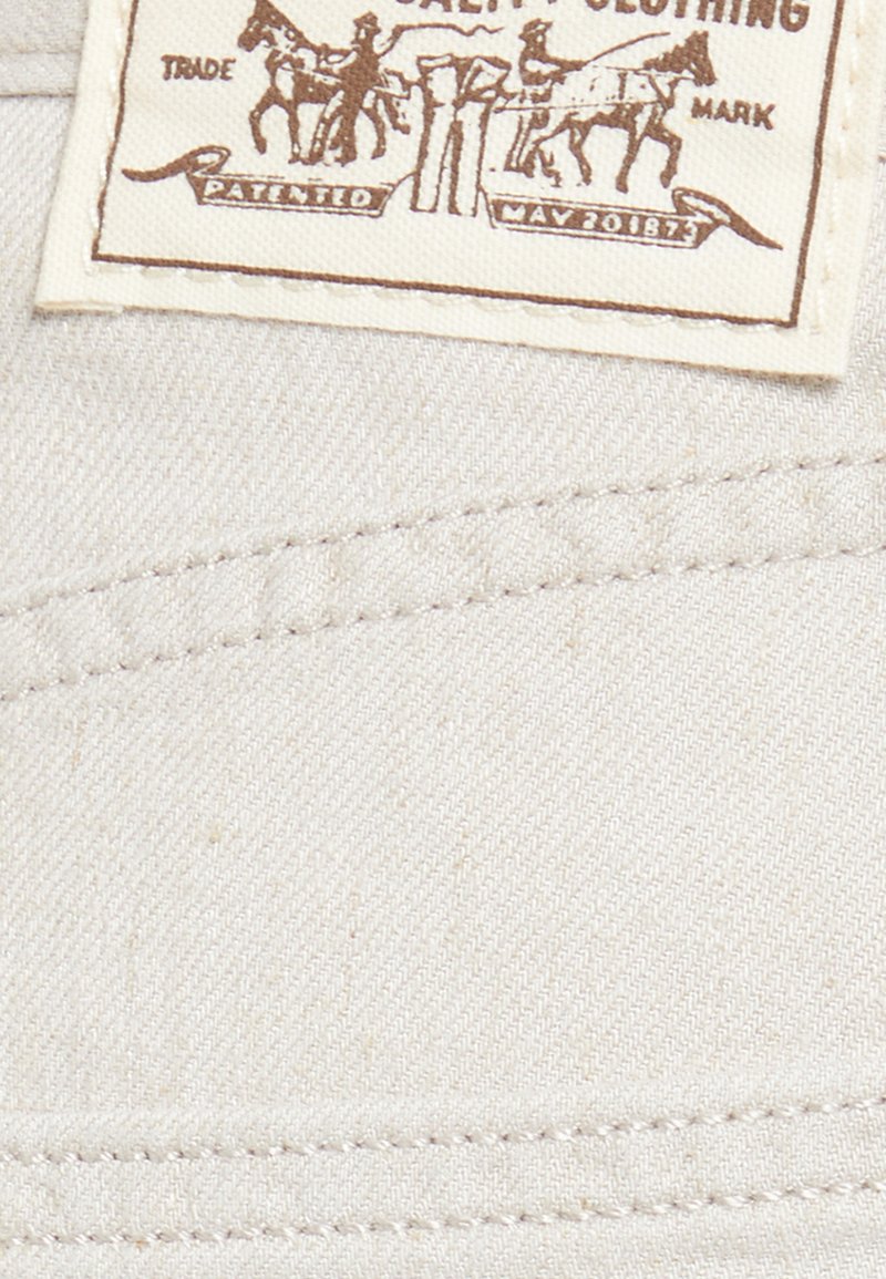 Weißes Stoffetikett mit braunem Text und Grafiken, das zwei Pferde und Reiter zeigt. Das Etikett enthält "Patented May 20187" und ein Warenzeichen.